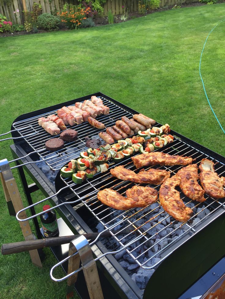 an outdoor grill with chicken, vegetables and other foods cooking on it's side