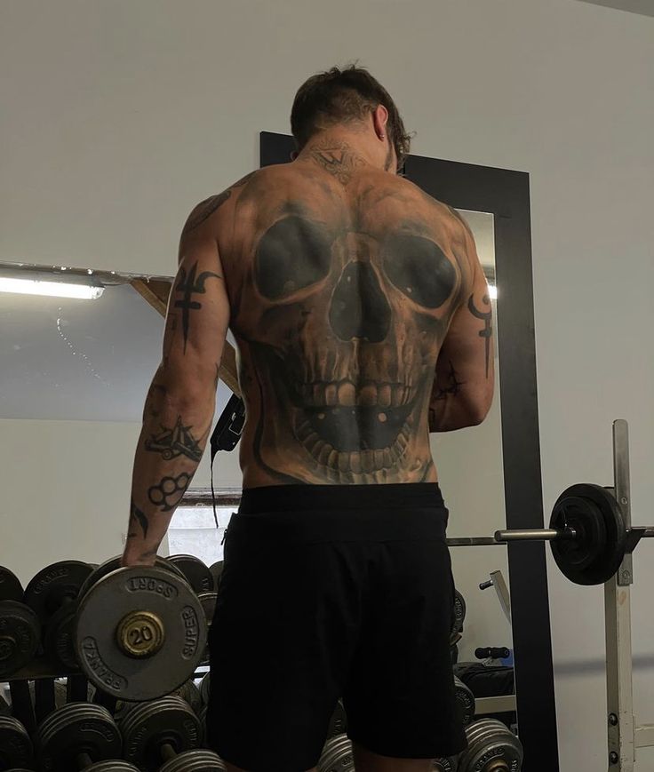 a man with tattoos on his back standing in front of a barbell