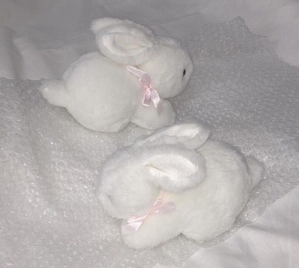 two white stuffed animals laying on top of a bed next to each other with pink bows