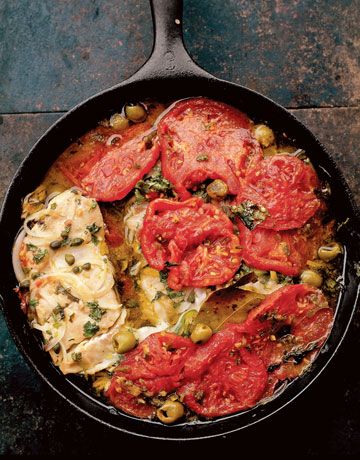 a skillet filled with meat and vegetables on top of a table next to a fork