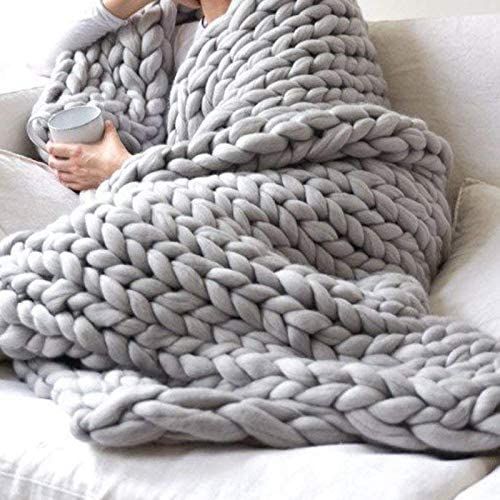 a person wrapped in a blanket on a couch holding a remote control and drinking from a cup