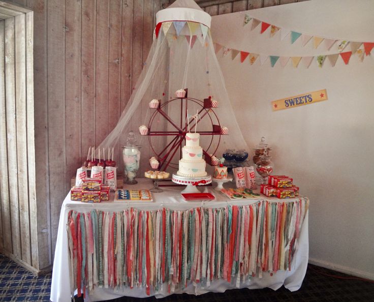 a table topped with lots of candy next to a ferris wheel and sign that says festas