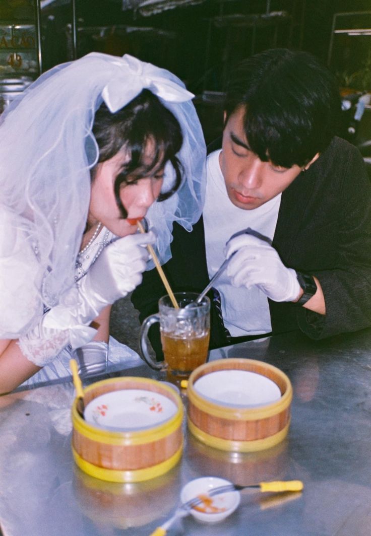 a bride and groom are sitting at a table with drinks in front of their faces