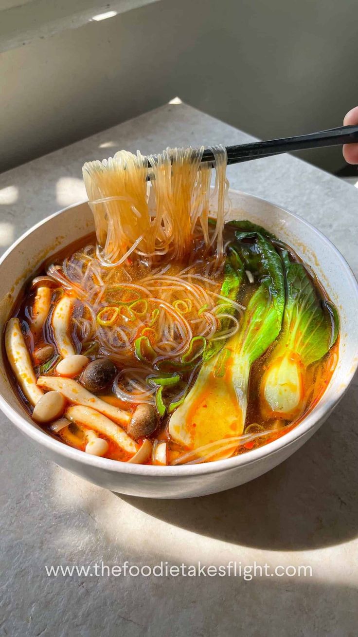 someone is holding chopsticks over a bowl of soup with noodles and broccoli