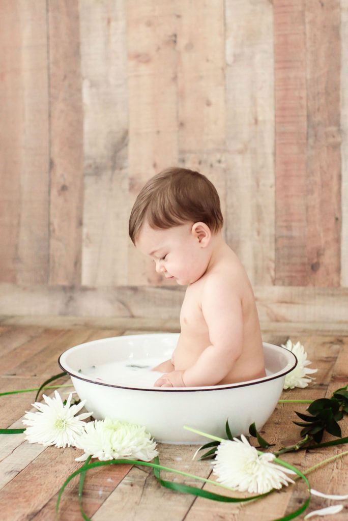 a baby is sitting in a bowl with flowers on the floor and looking at it