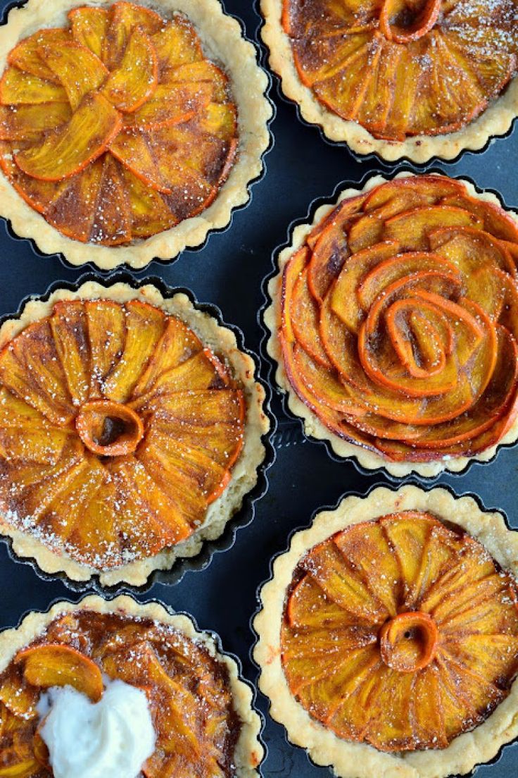 four pies with icing sitting on top of a black tray next to each other