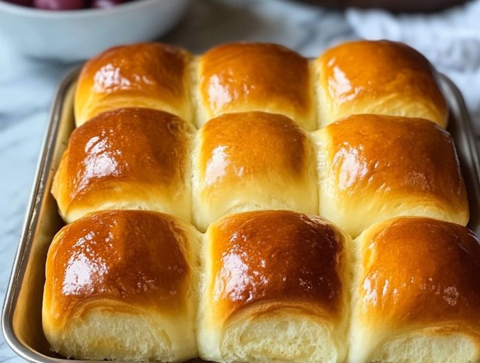 a baking pan filled with freshly baked rolls and cherries in the bowl behind it