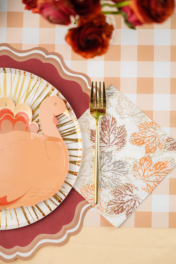 a plate with a turkey on it next to a fork and flower arrangement in the background