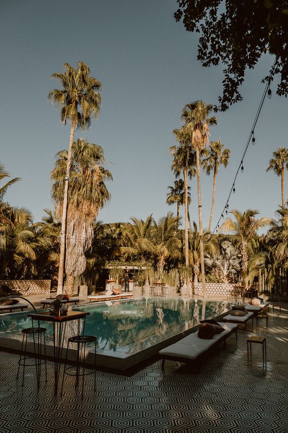 an empty pool surrounded by palm trees and lounge chairs in the middle of the day