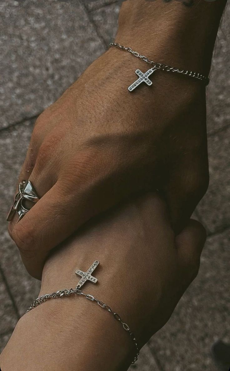 two people holding hands with cross bracelets on their wrists and one is wearing a ring