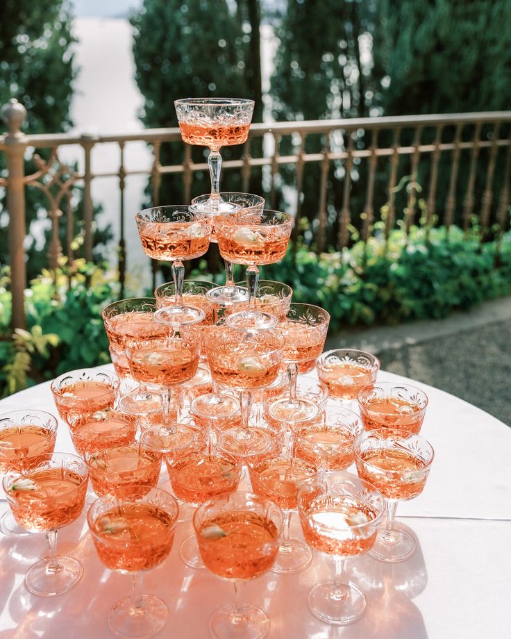 a table topped with lots of wine glasses on top of a white table covered in greenery