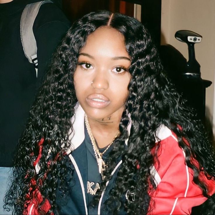 a woman with long black curly hair wearing a red and white jacket looking at the camera