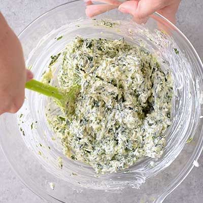 someone is mixing spinach in a glass bowl