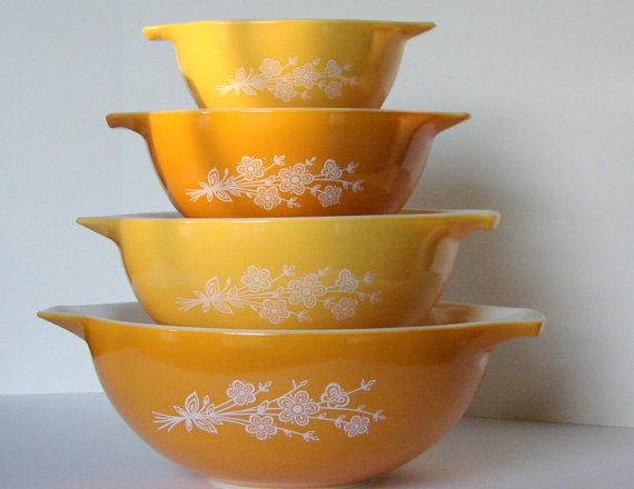 four yellow bowls stacked on top of each other with white flowers and leaves painted on them