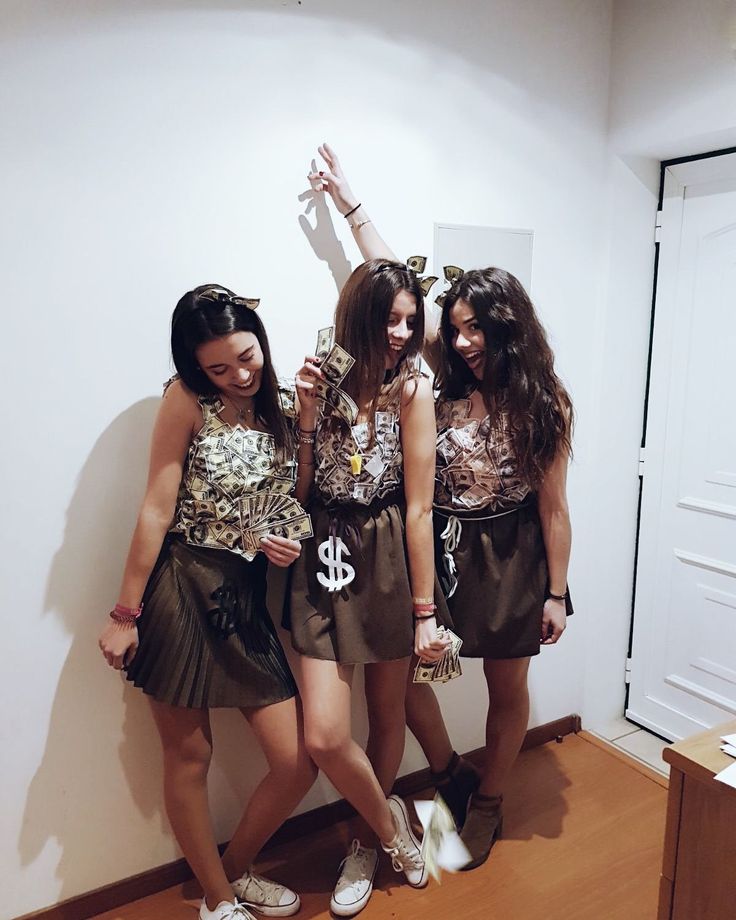 three young women standing next to each other in front of a wall holding up their cell phones