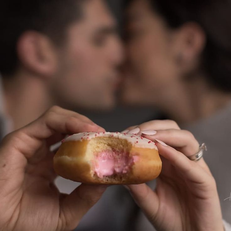 a man and woman kissing while holding a doughnut with frosting on it's side