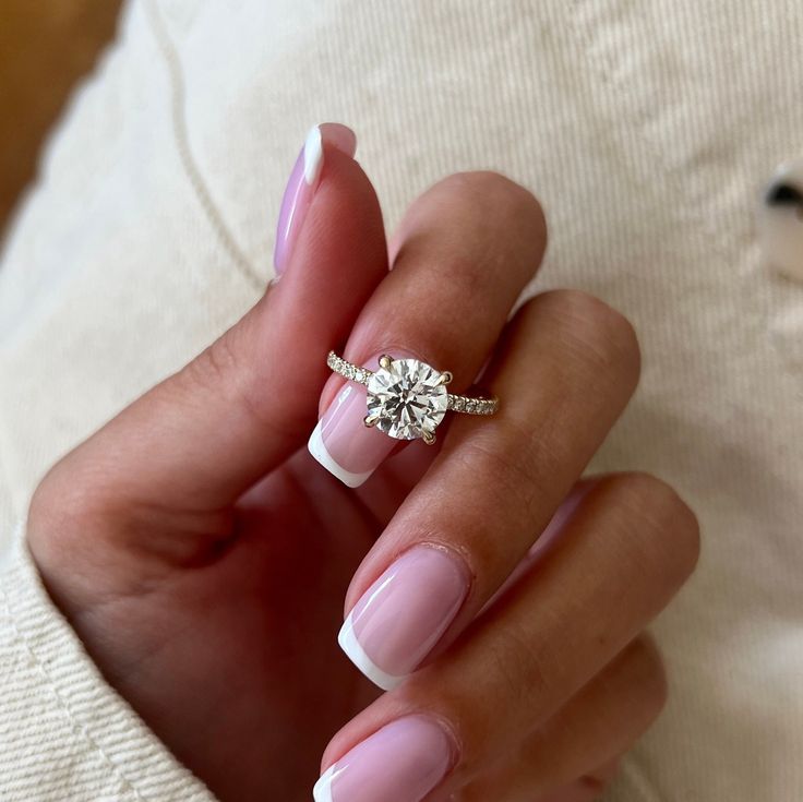 a woman's hand with pink and white nail polish holding a diamond ring