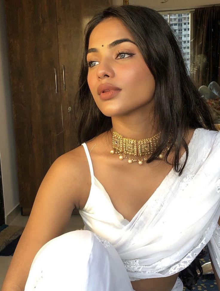 a woman wearing a white sari and gold choker is posing for the camera