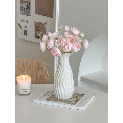 a white vase filled with pink roses sitting on top of a table next to a candle