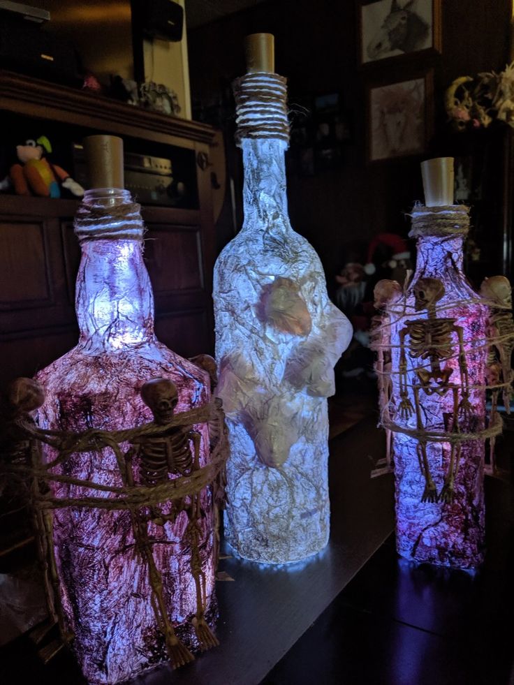 three bottles with lights in them sitting on a table next to other bottles and baskets