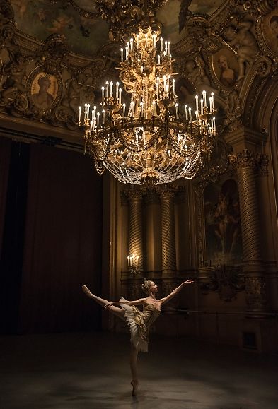 a ballerina is standing in front of a chandelier