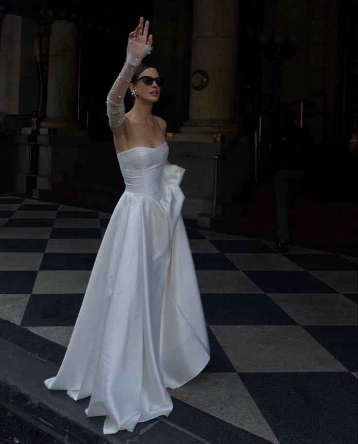 a woman in a white wedding dress waves to the crowd while standing on a black and white checkered floor