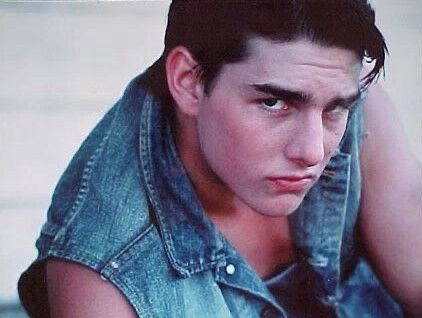 a young man wearing a denim vest and looking at the camera with his hand on his hip