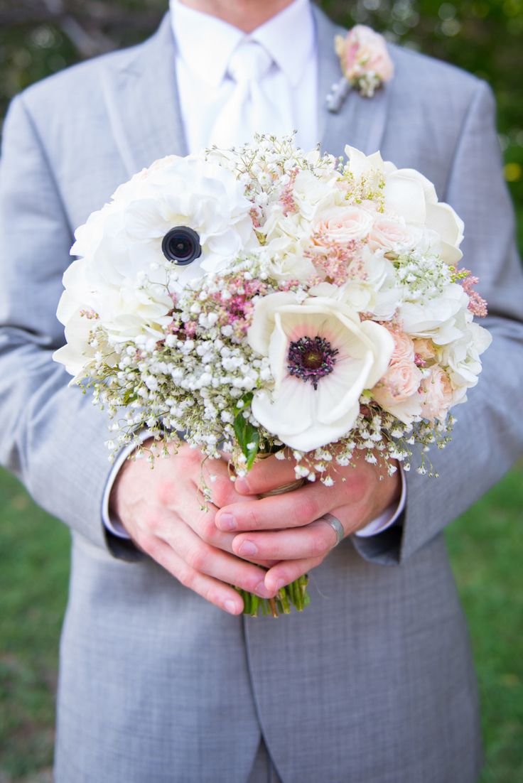 a man in a gray suit holding a bouquet of white and pink flowers on his lapel