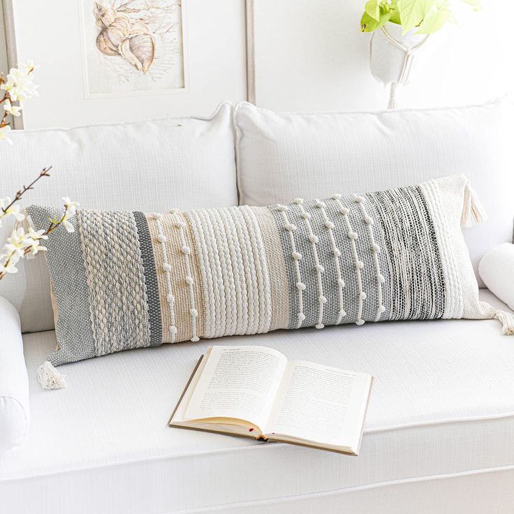 a white couch with a book, cup and vase on it next to an open book