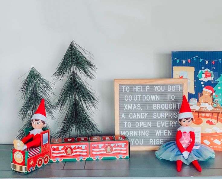 two elfs sitting on top of a shelf next to a train and christmas tree