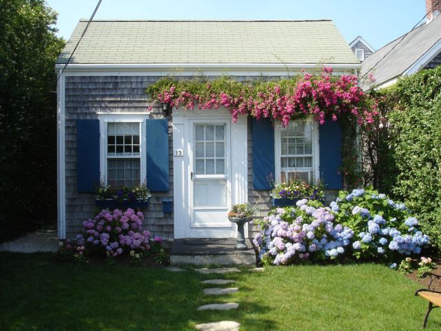 a house with blue shutters and flowers in the front yard