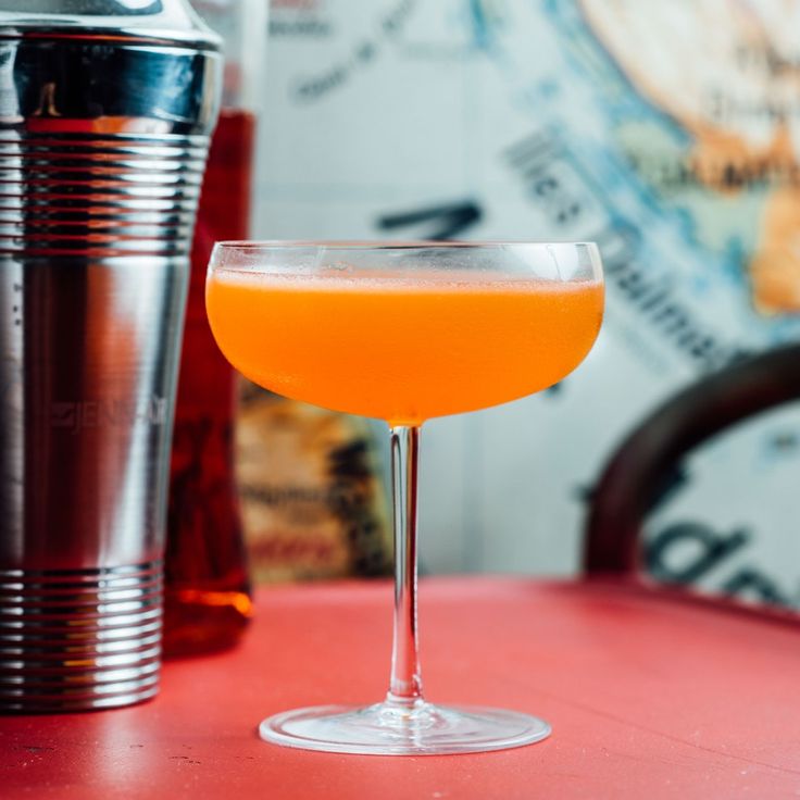 an orange drink sitting on top of a pink table