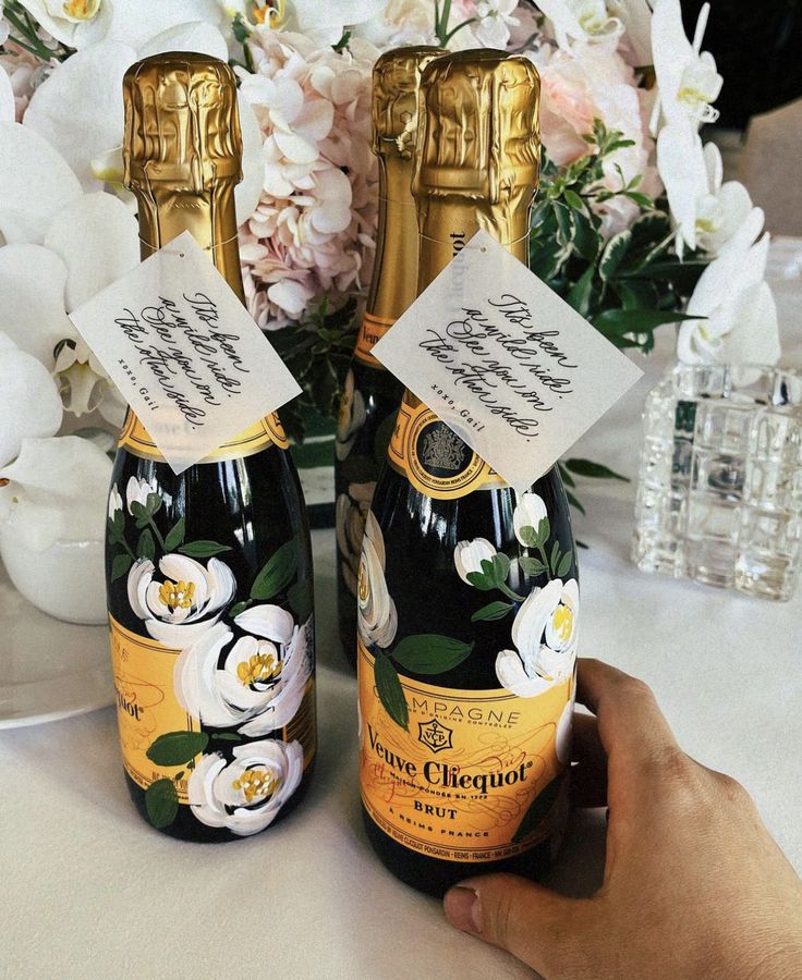 two bottles of champagne are sitting on a table with flowers and vases in the background