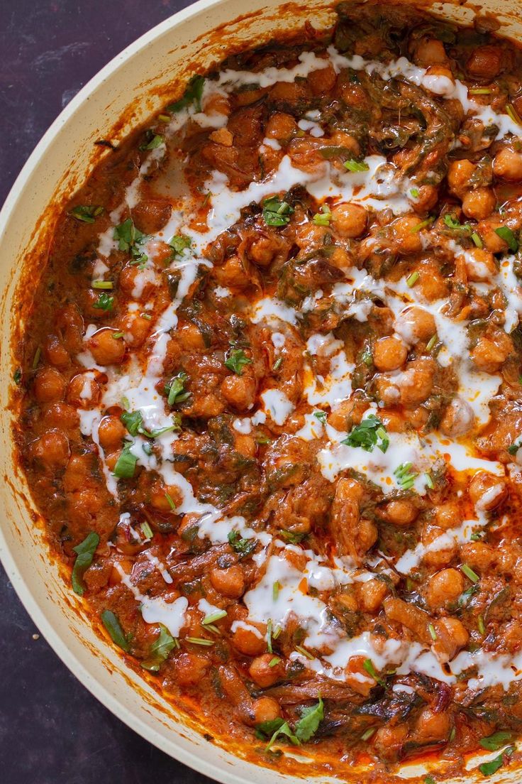 a large bowl filled with lots of food on top of a purple tablecloth covered in white sauce