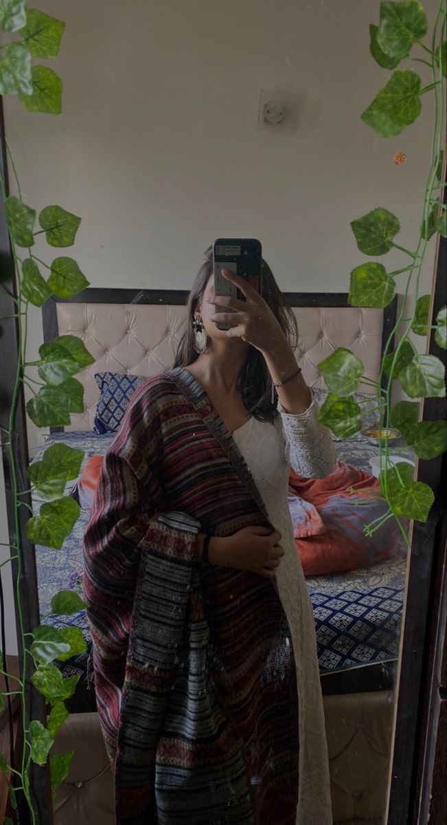 a woman taking a selfie in front of a bed with ivy growing on it