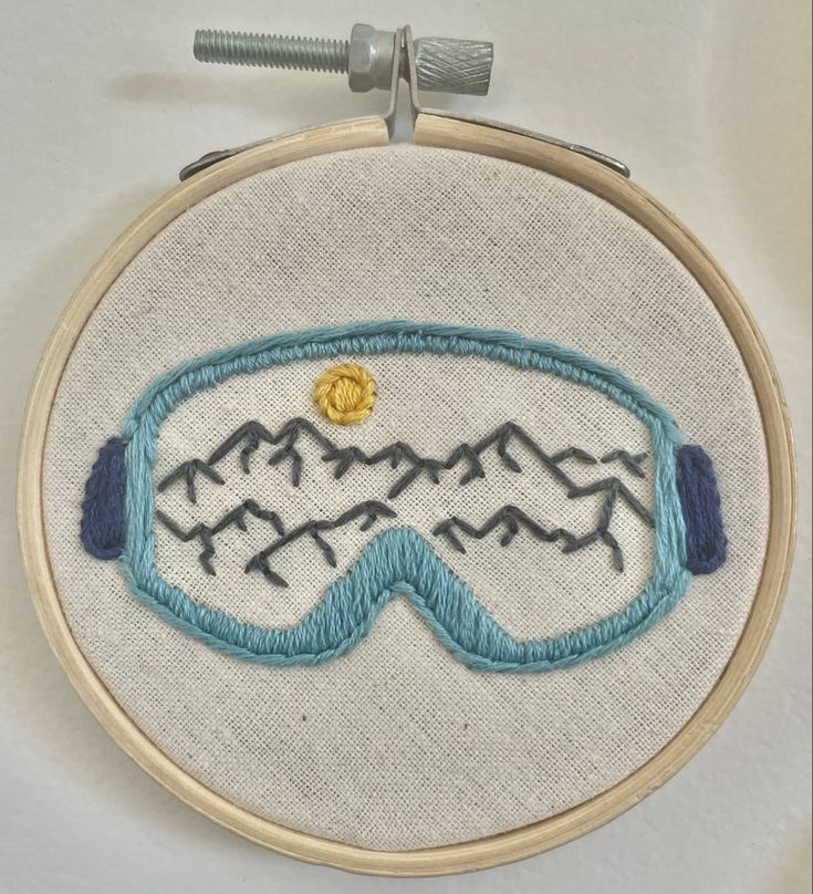 a close up of a embroidery on a white surface with a blue frame and mountains in the background