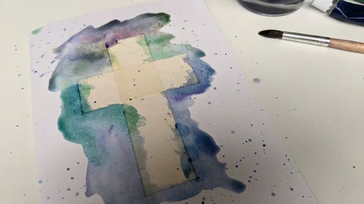 a cross painted on top of a piece of paper next to some paintbrushes