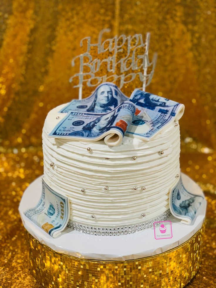 a white cake with money on top is sitting on a gold sequin tablecloth