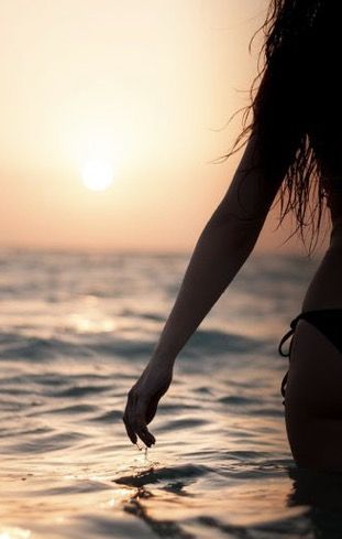 a woman standing in the ocean at sunset with her hand on the water's edge