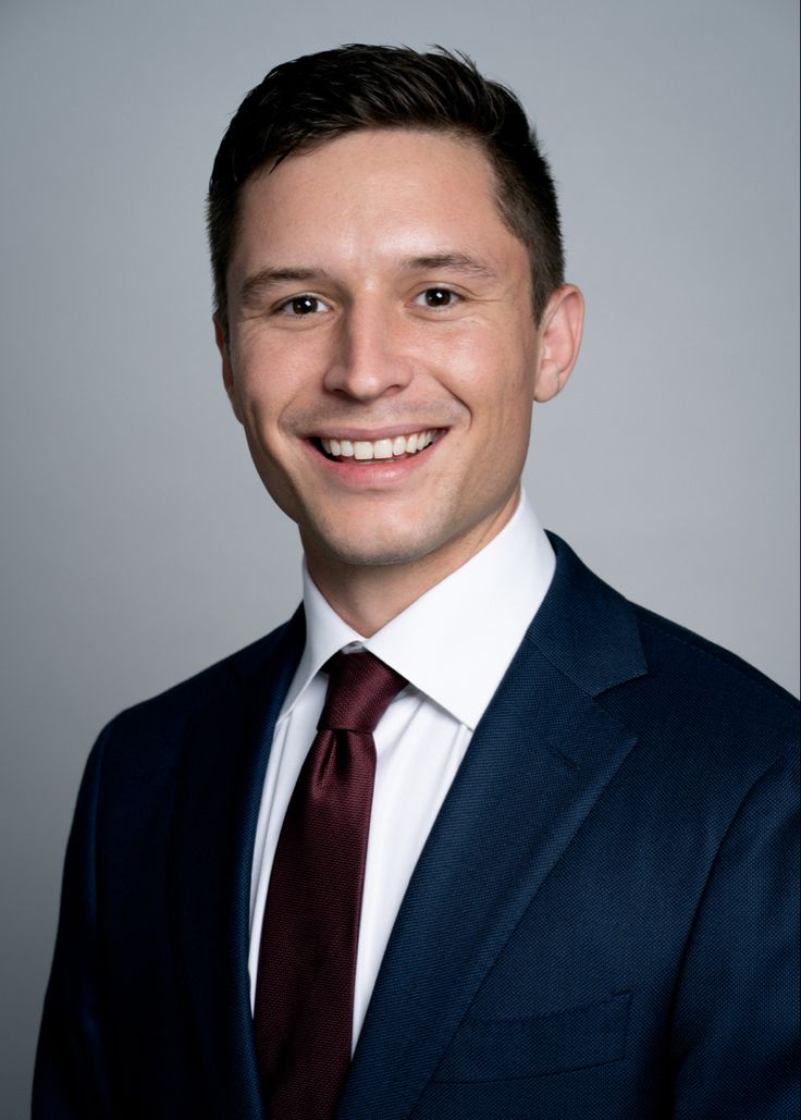 a man in a suit and tie smiling at the camera while wearing a red tie