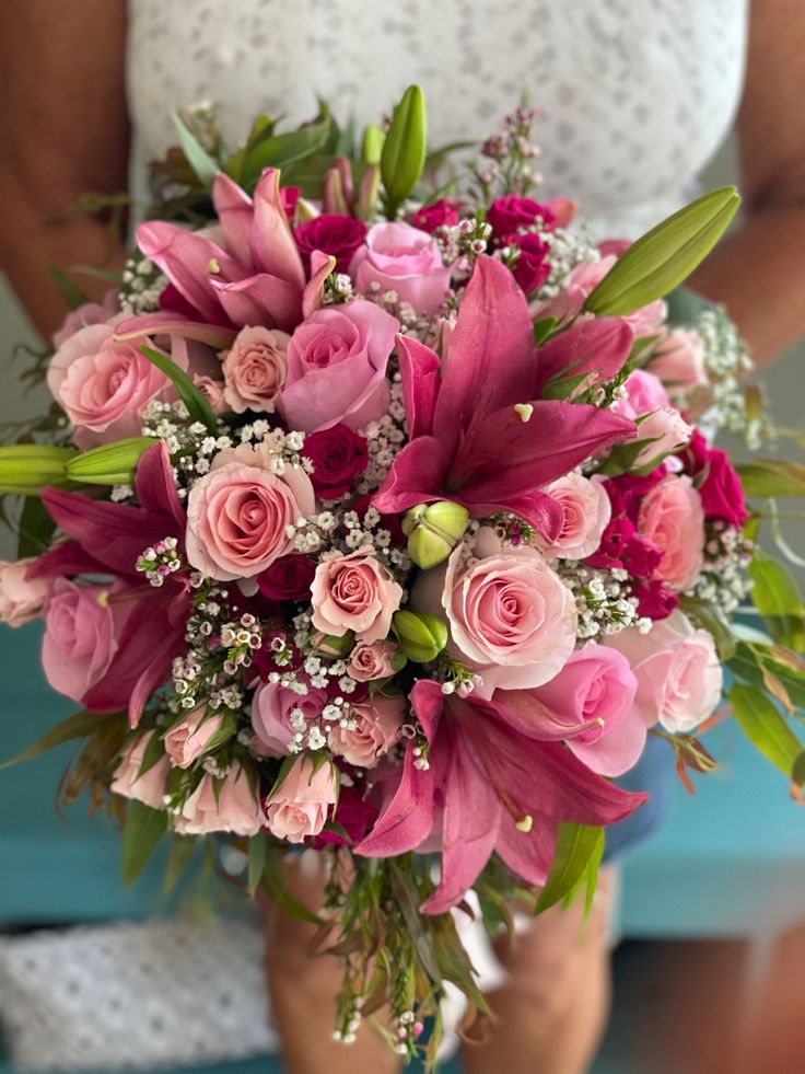 a bridal bouquet with pink roses and baby's breath is held by a woman