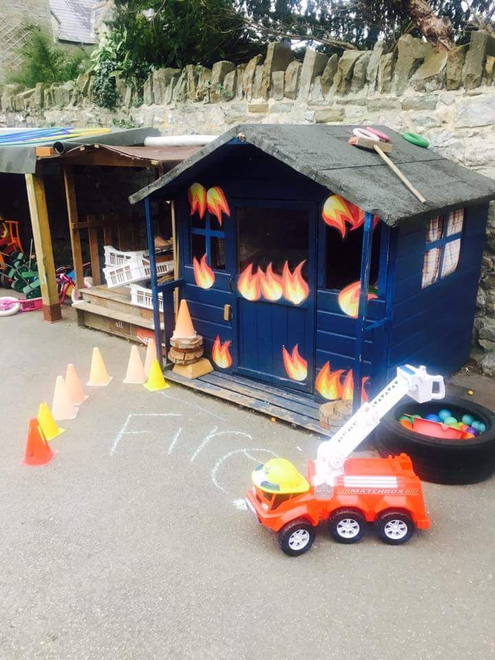 a toy fire truck is parked in front of a blue shed with flames painted on it