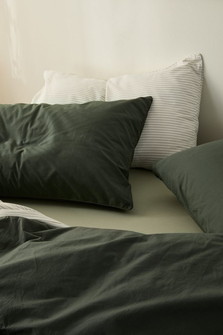 a bed with green sheets and pillows on top of it in front of a white wall