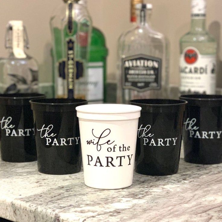 four black cups sitting on top of a counter with liquor bottles in the back ground