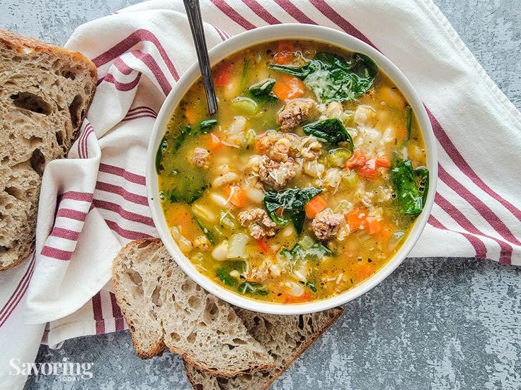 a bowl of soup with meat, vegetables and bread on a towel next to it