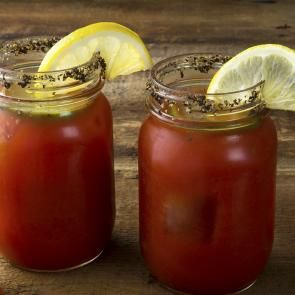 two mason jars filled with tomato sauce and garnished with lemon wedges on a wooden table