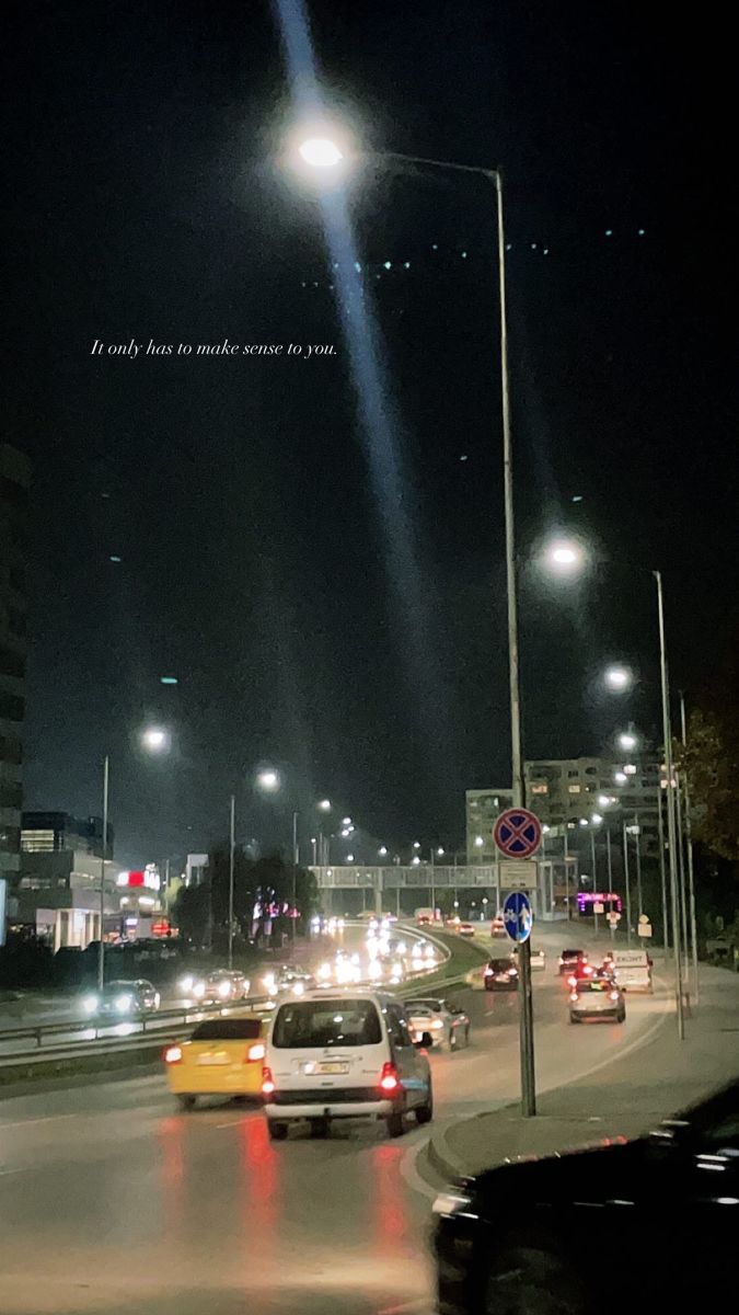 cars driving down the road at night with street lights in the background and an advertisement above them