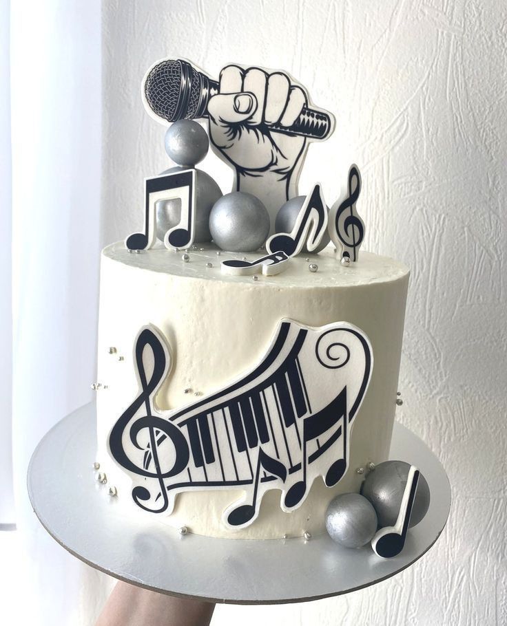 a white cake with black and silver music notes on it, topped with a microphone