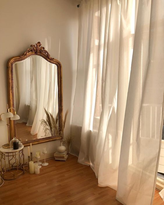 there is a mirror and some candles in front of a window with curtains on it