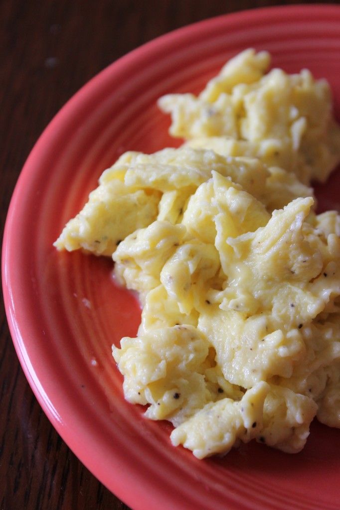 scrambled eggs on a red plate sitting on a wooden table